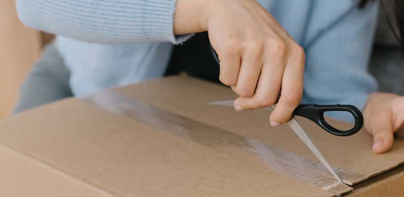 A person opening a taped cardboard box with scissors