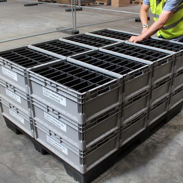 A person stacking automotive packaging containers in a warehouse.