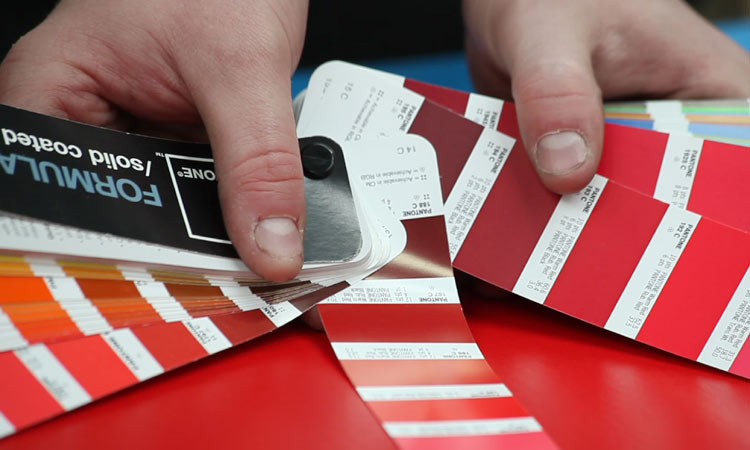 Quality standards A person checking the colour of printed cardboard packaging with a Pantone book