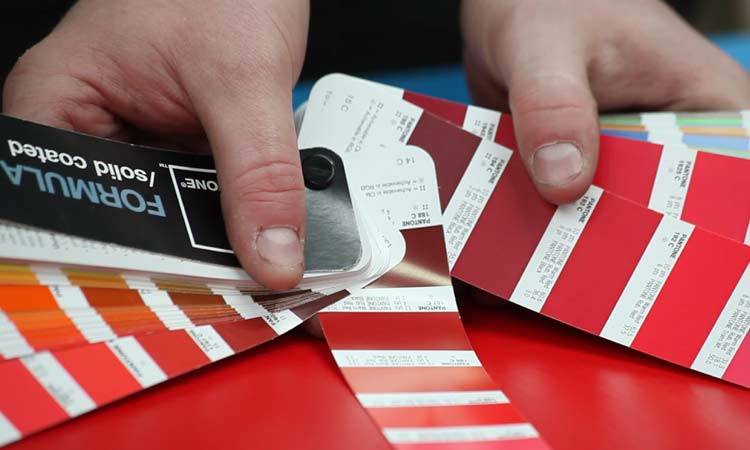 A person checking the colour of coated cardboard with a Pantone book.